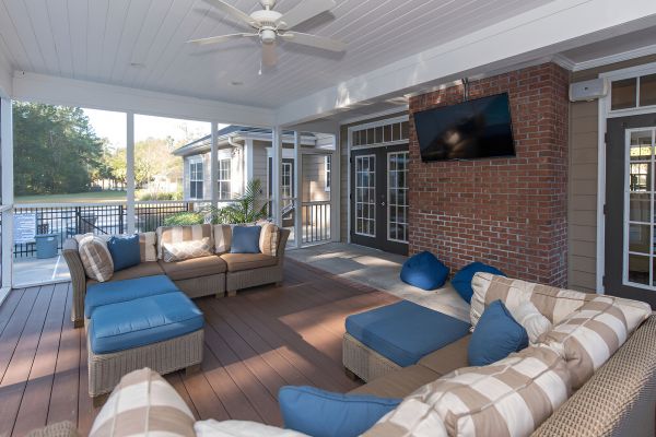 Cedar Grove apartment homes with Screened patio with wicker sofas, a ceiling fan, TV, and bean bags, overlooking a green outdoor area.