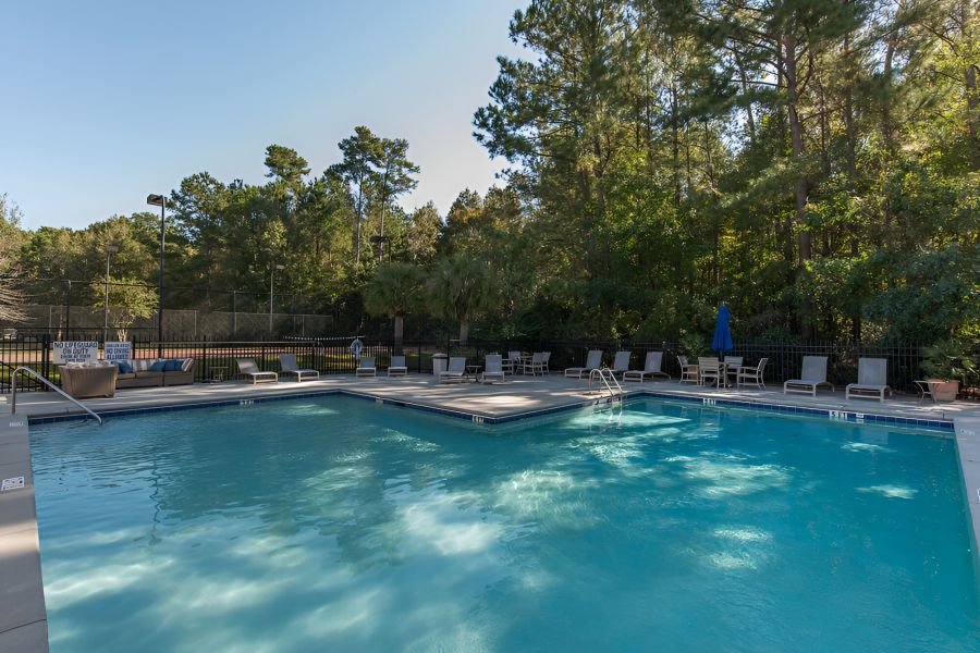 Cedar Grove apartment homes with an Outdoor swimming pool surrounded by lounge chairs and trees, with a tennis court in the background.