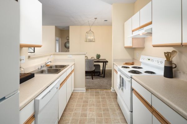 Cedar Grove Modern kitchen with white cabinets, beige countertops, and a view into a carpeted dining area with a table and chairs.
