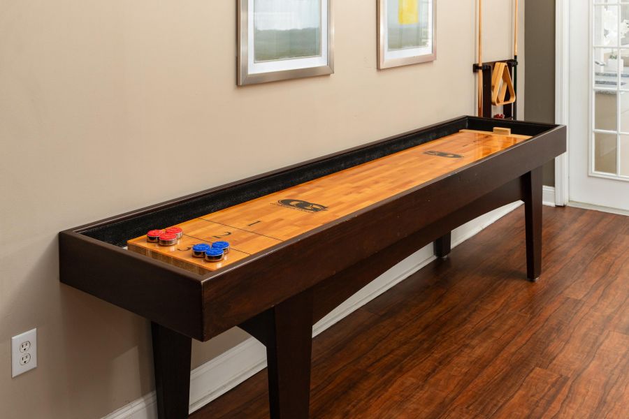 Cedar Grove apartment homes with A shuffleboard table with pucks on one end, set in a room with wood floors and wall art above.