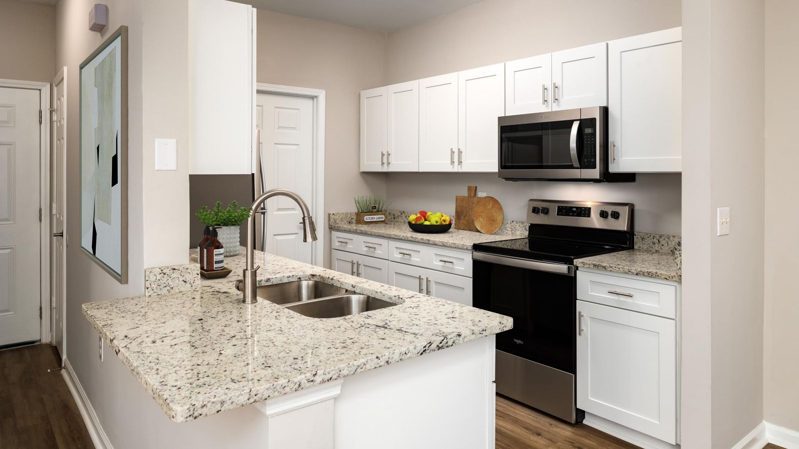 Modern kitchen and living area with white cabinets, stainless steel appliances, and a large island. Cozy seating area with a sofa and rug in the background. Bright and inviting atmosphere.