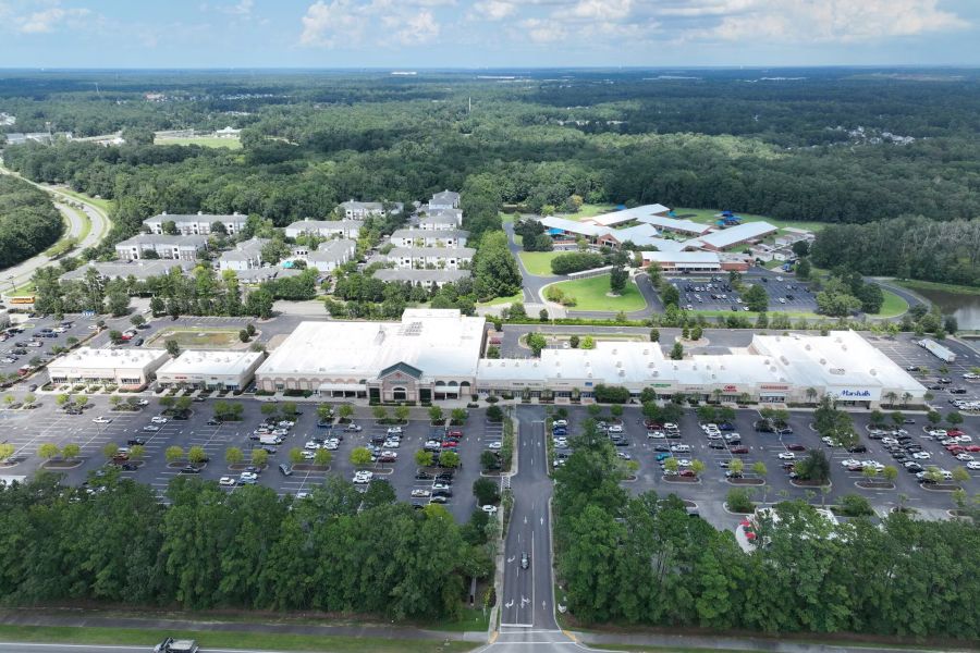 Cedar Grove Aerial view of a shopping center with a large parking lot, surrounded by trees and nearby buildings.
