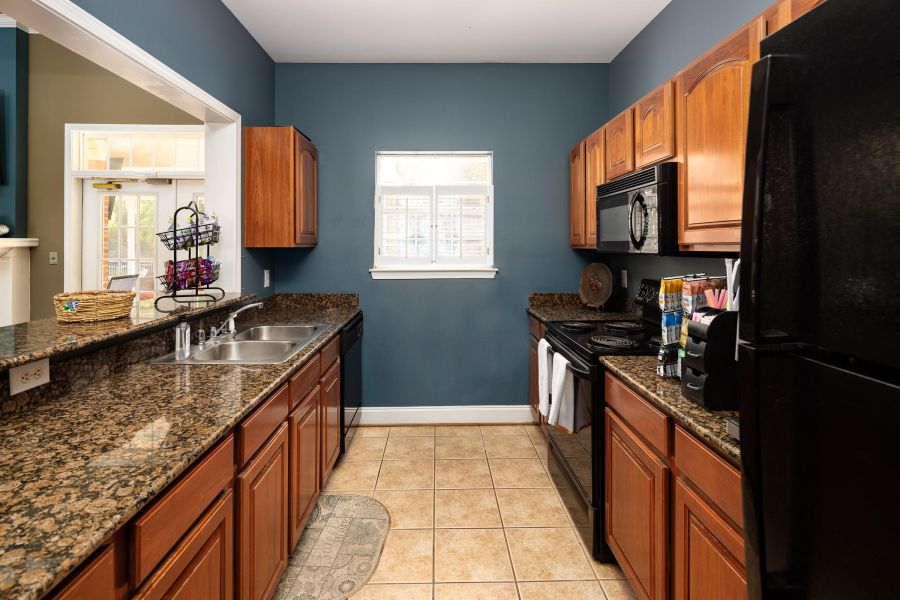 Cedar Grove apartment homes with A kitchen with wood cabinets, granite countertops, black appliances, and a window above the sink.