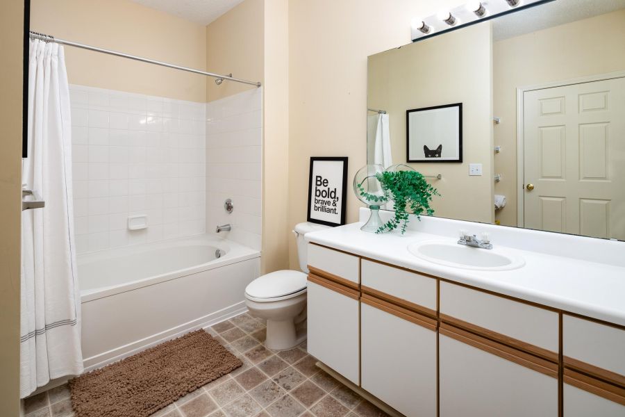Cedar Grove apartment homes with Modern bathroom with a bathtub, white shower curtain, large mirror, and plants on the counter.