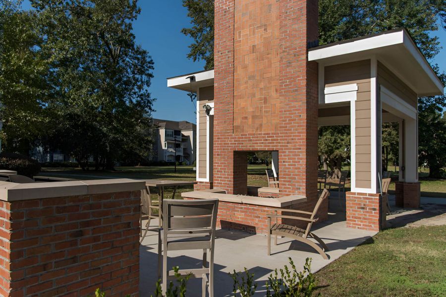 Cedar Grove apartment homes with Outdoor patio with chairs around a brick fireplace under a covered structure, surrounded by trees.