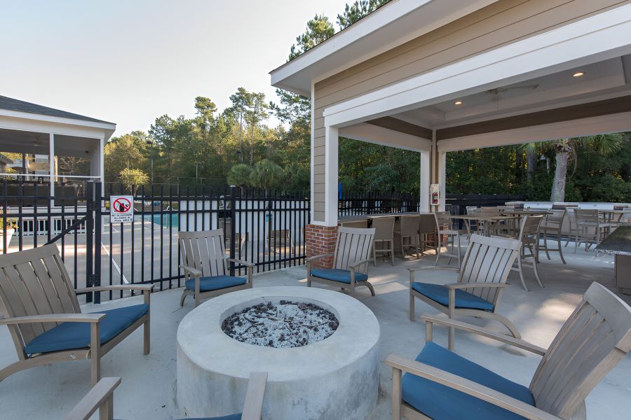 Cedar Grove apartment homes with Outdoor seating area with wooden chairs around a fire pit, next to a covered patio and fenced pool area.