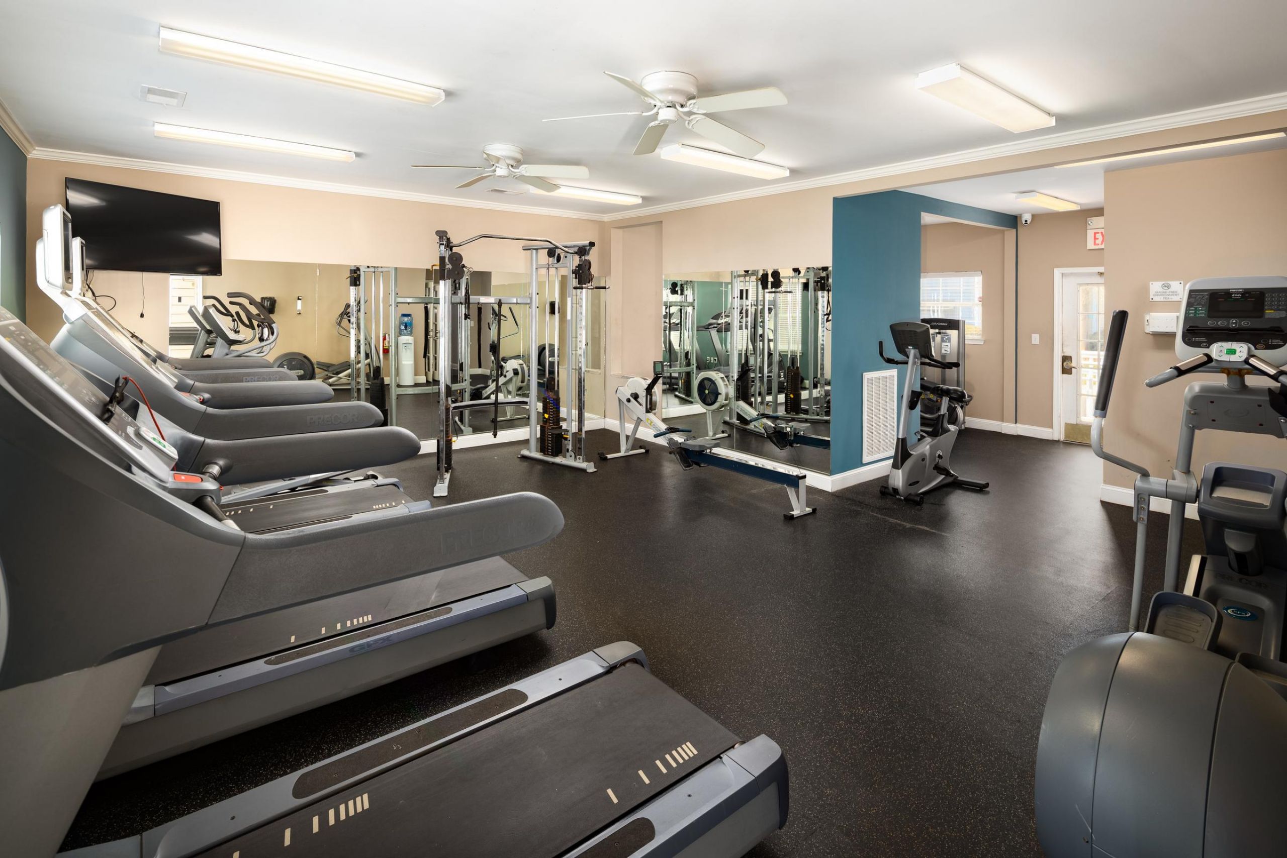 Cedar Grove apartment homes with Modern gym with treadmills, exercise bikes, weight machines, mirrors, and bright overhead lighting.