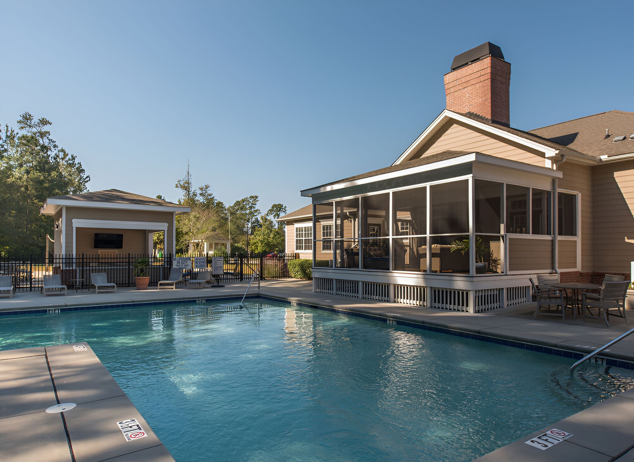 Cedar Grove apartment homes with Outdoor swimming pool beside a house with a screened porch and a covered patio, under a clear blue sky.